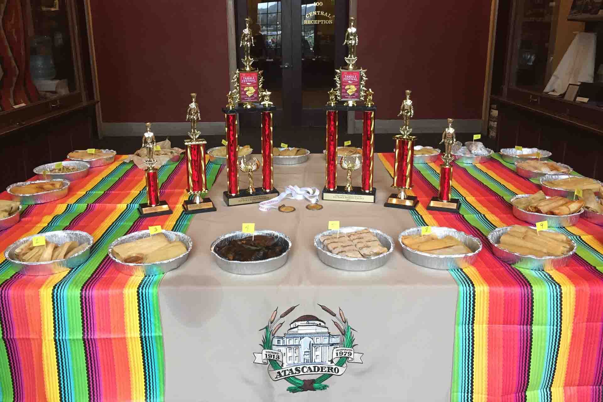 Image of tamale platters and trophies displayed on a table with colorful table runners.