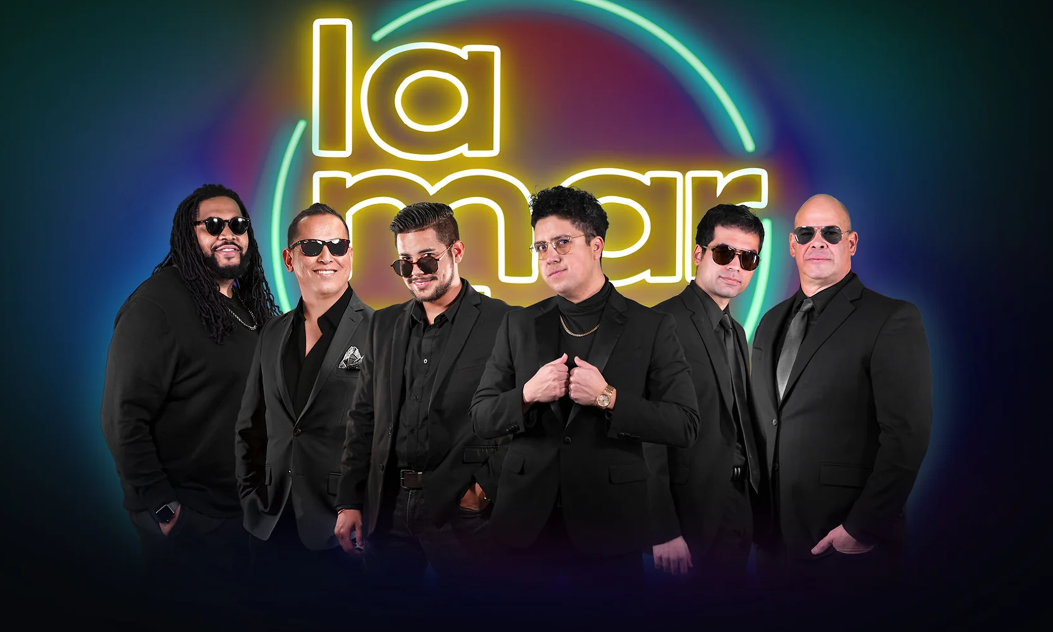 Image of six men, La Marcha Sound members, in black dress jackets with a neon sign of their band name behind them.